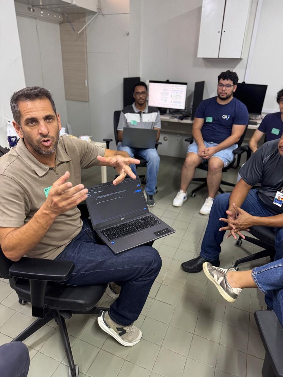 Professor gesticula explicando algo a participantes sentados em frente a computadores em laboratório do HUB.